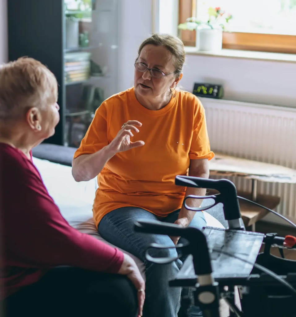 Två kvinnor sitter på en sängkant och pratar.